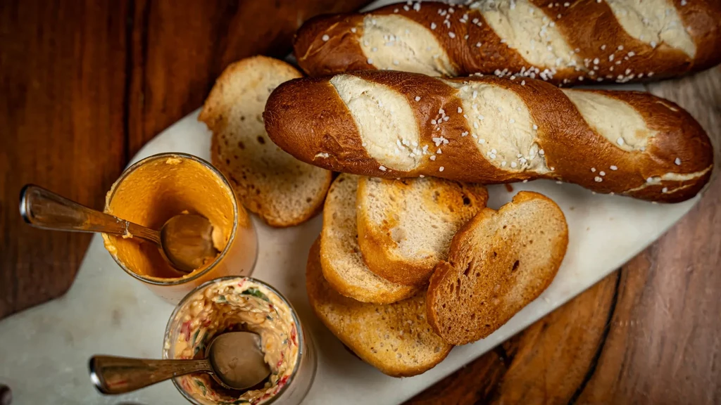 Twisted salted pretzel bread, toasted baguette slices, and two dips.