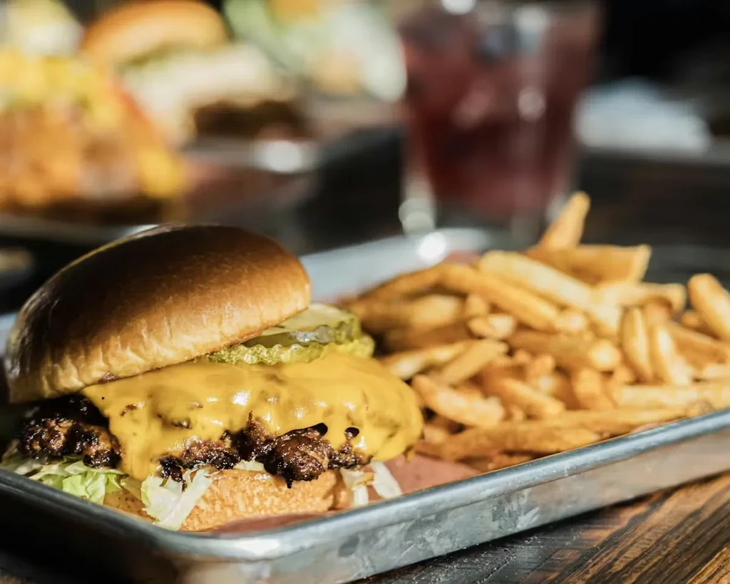 Close-up of cheeseburger, melted cheese, fries, on metal tray.