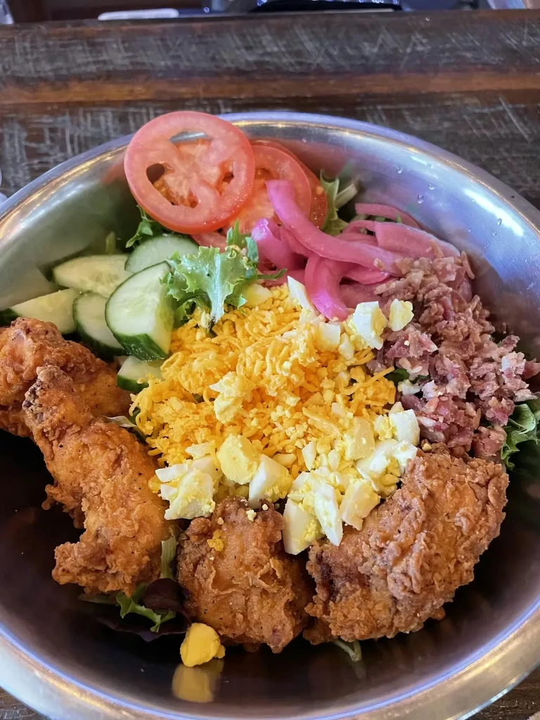 Hearty fried chicken salad with lettuce, tomatoes, cheese, and pickled onions.