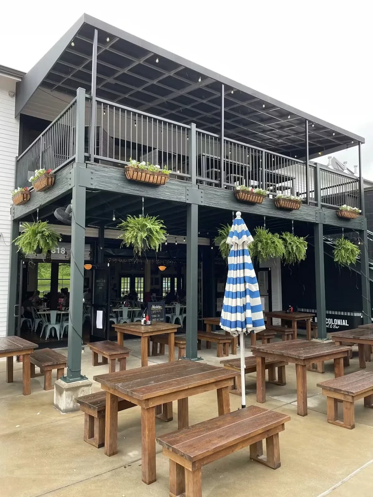 Exterior of a two-story restaurant with outdoor dining, flowers, and umbrella.