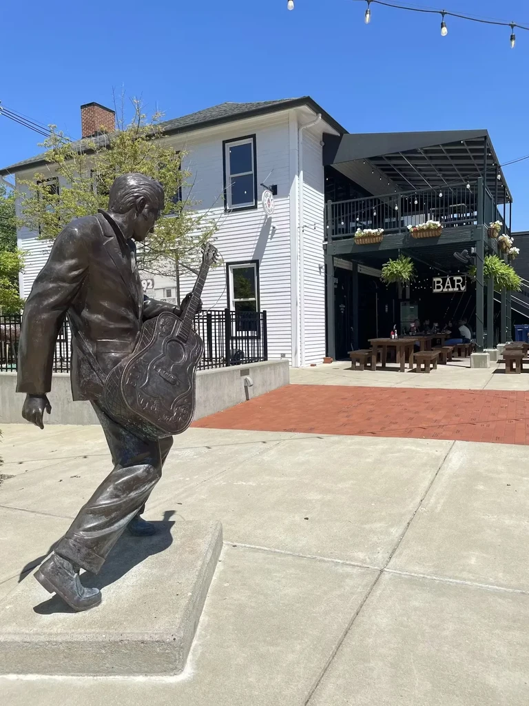 Bronze statue of a man holding a guitar, in front of a bar.