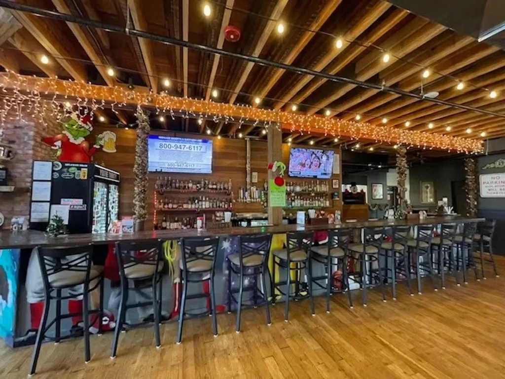 Festive bar interior with Grinch cutout, Christmas tree, and string lights.
