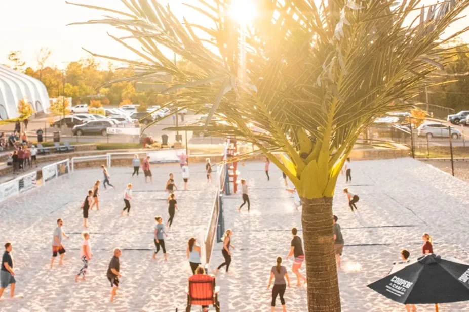 Golden hour sunlight illuminates sand volleyball courts filled with active players.