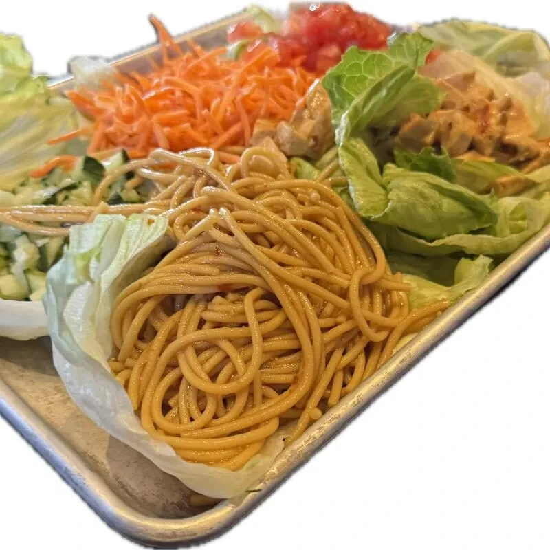 Deconstructed Asian meal with noodles, chicken, and vegetables in lettuce cups.