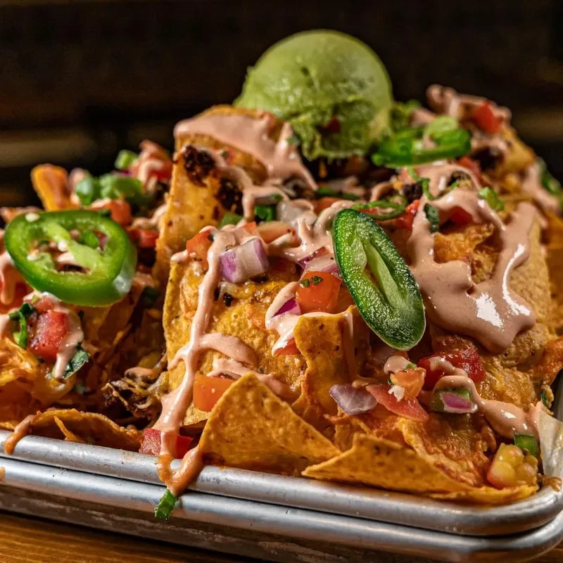Mound of nachos on a tray with cheese, pico, jalapeños, and guacamole.
