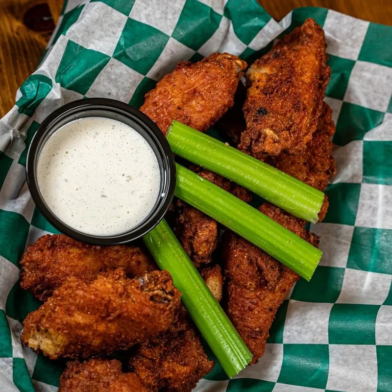 Basket of crispy fried chicken wings, celery, and dipping sauce.