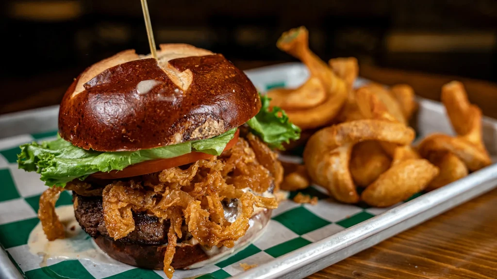 Gourmet burger on a pretzel bun, fried onions, and potato wedges.