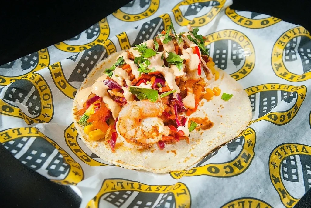 Shrimp taco with slaw, sauce, cilantro, on Louisville Taco City paper.