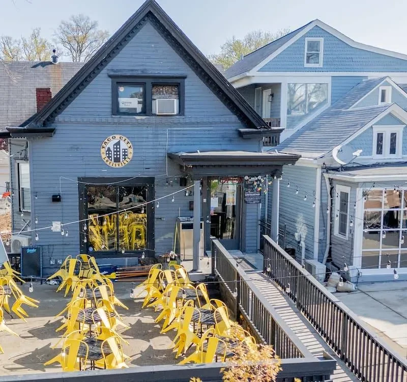 Blue-grey Taco City Louisville restaurant and empty patio with yellow chairs.