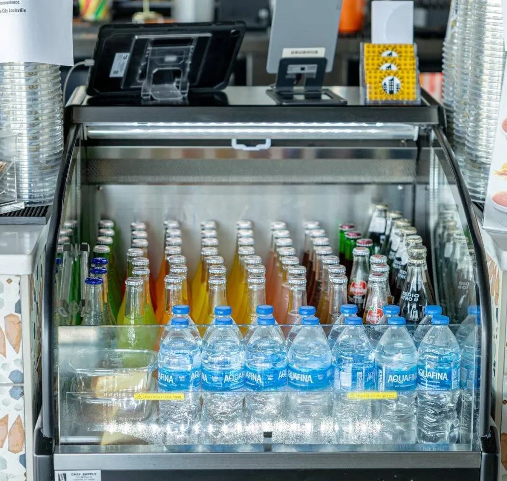 Display case with bottled water, colorful sodas, and POS systems.