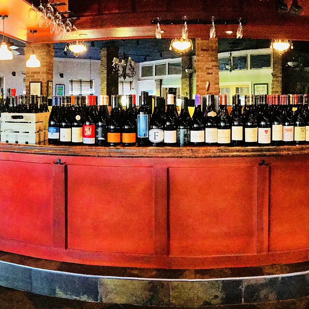 Well-stocked restaurant bar with many red wine bottles and hanging glasses.