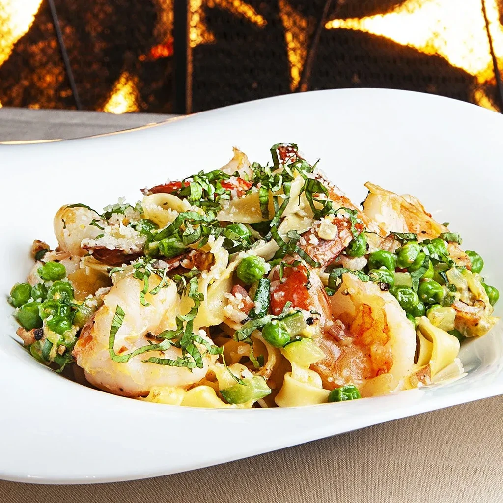 Close-up of pasta with shrimp, green peas, herbs, and grated cheese.
