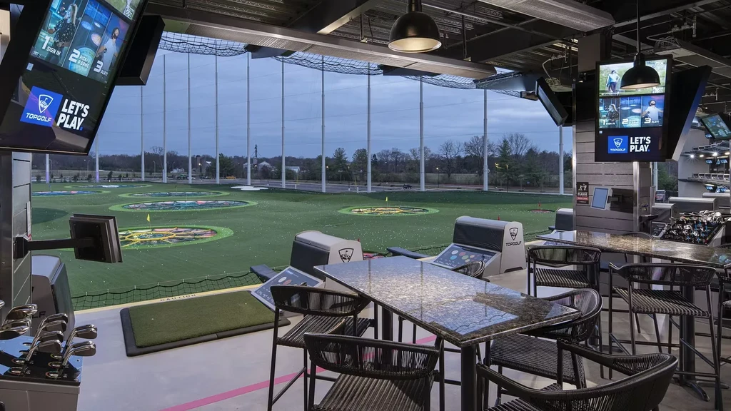 Topgolf bay showing high-top tables, golf hitting area, and outdoor range.
