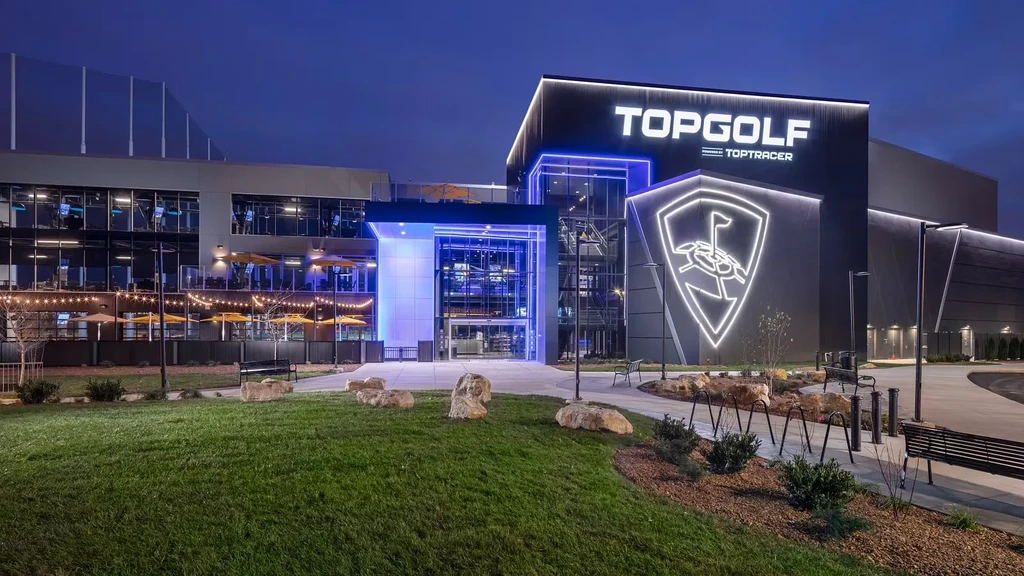 Illuminated modern Topgolf complex at night with a blue entrance.