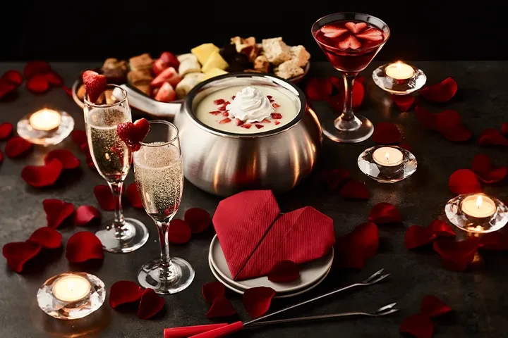 Romantic fondue spread with champagne, cocktails, candles, and rose petals.
