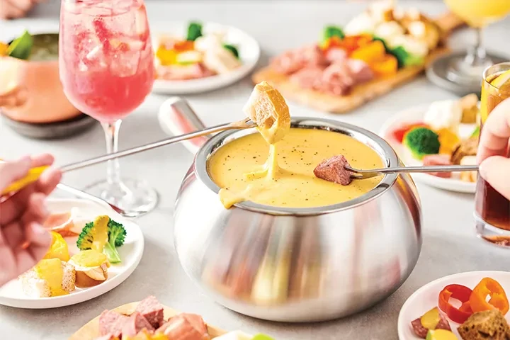 People dipping bread, meat, and vegetables into a cheese fondue pot.
