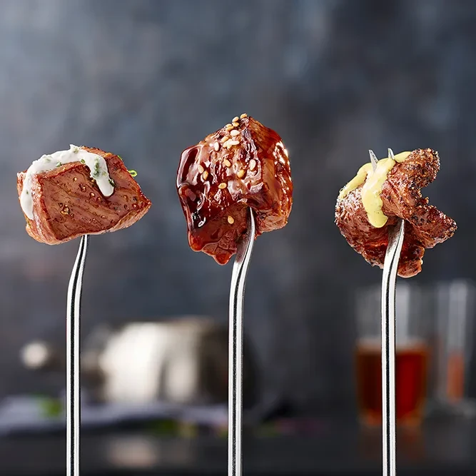 Three meat pieces on fondue forks, each with different toppings.