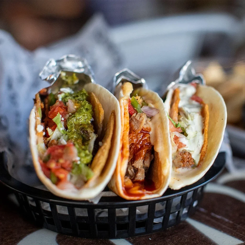 Close-up of three distinct tacos with colorful fillings in a black basket.