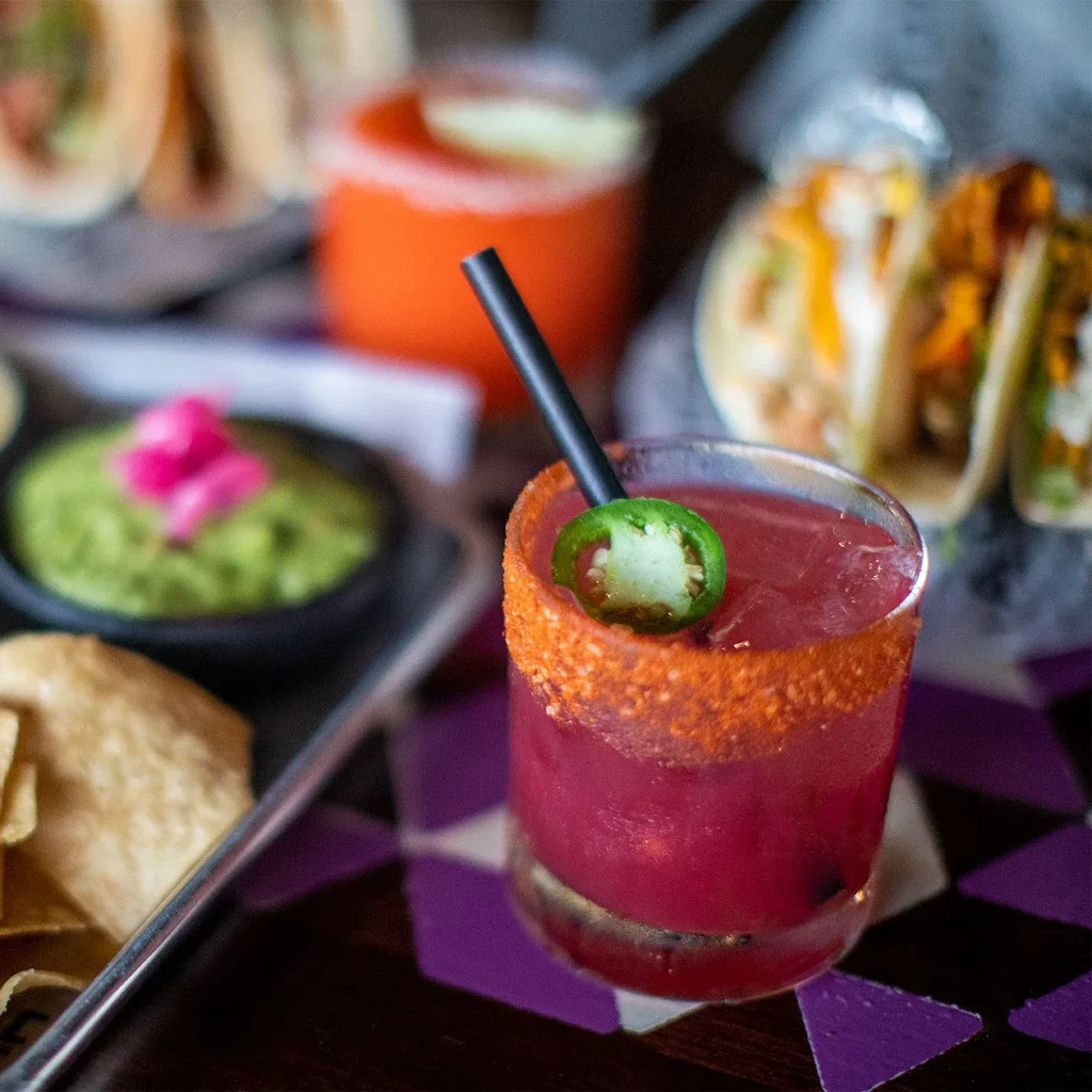 Pink cocktail with chili-salt rim, jalapeño slice, and black straw.