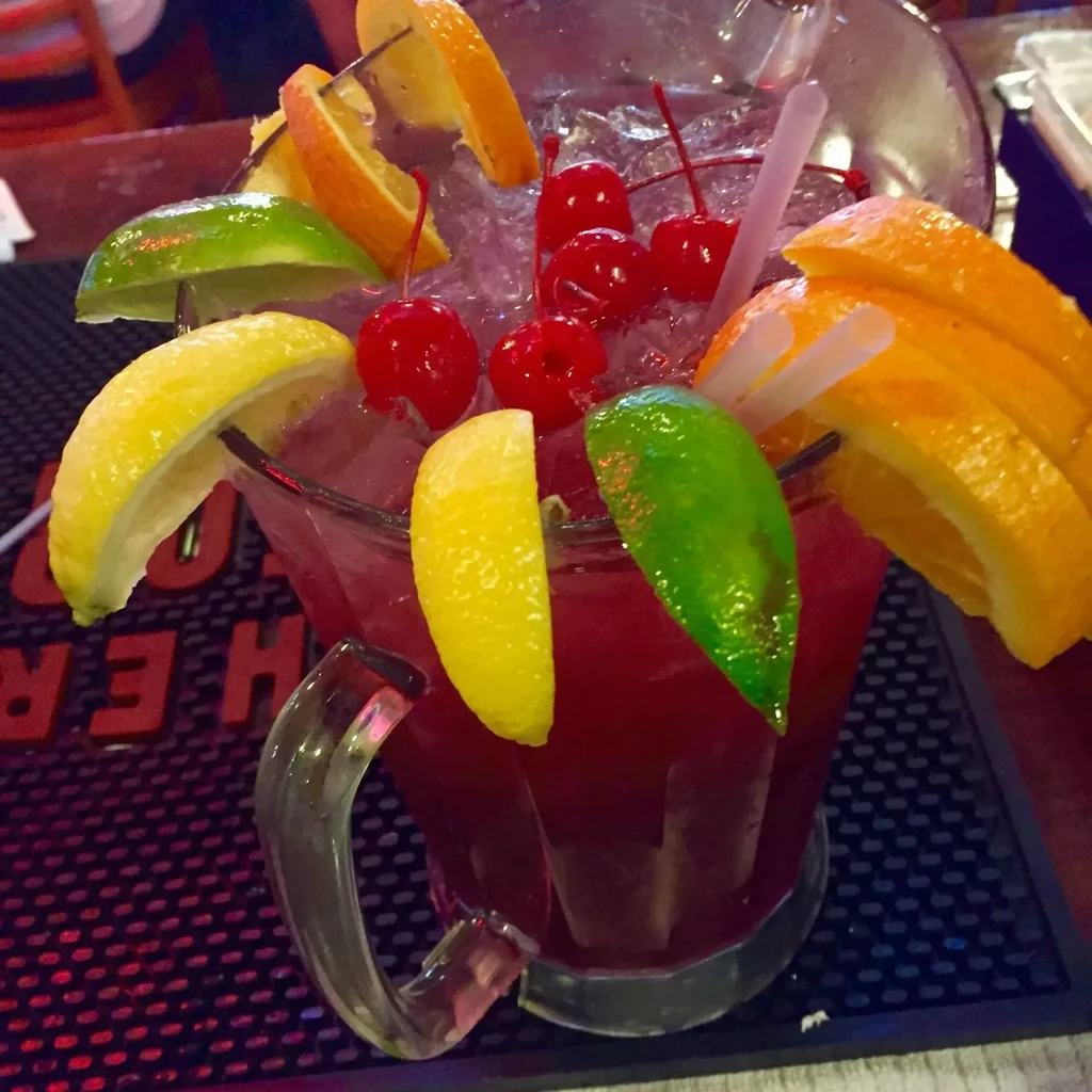 Clear glass pitcher with iced purple drink, cherries, citrus, and straws.