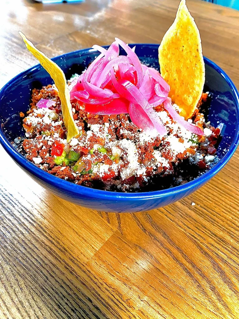 Colorful Mexican bowl with guacamole, meat, pickled onions, cheese, chips.