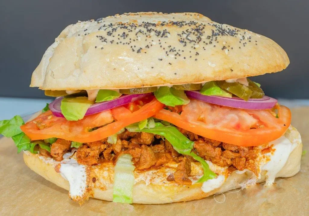 Large sandwich with meat, vegetables, and sauce on a poppy seed bun.