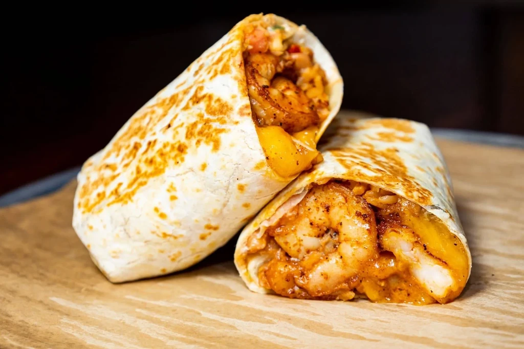 Diagonally sliced shrimp burritos displaying shrimp, rice, and orange sauce.