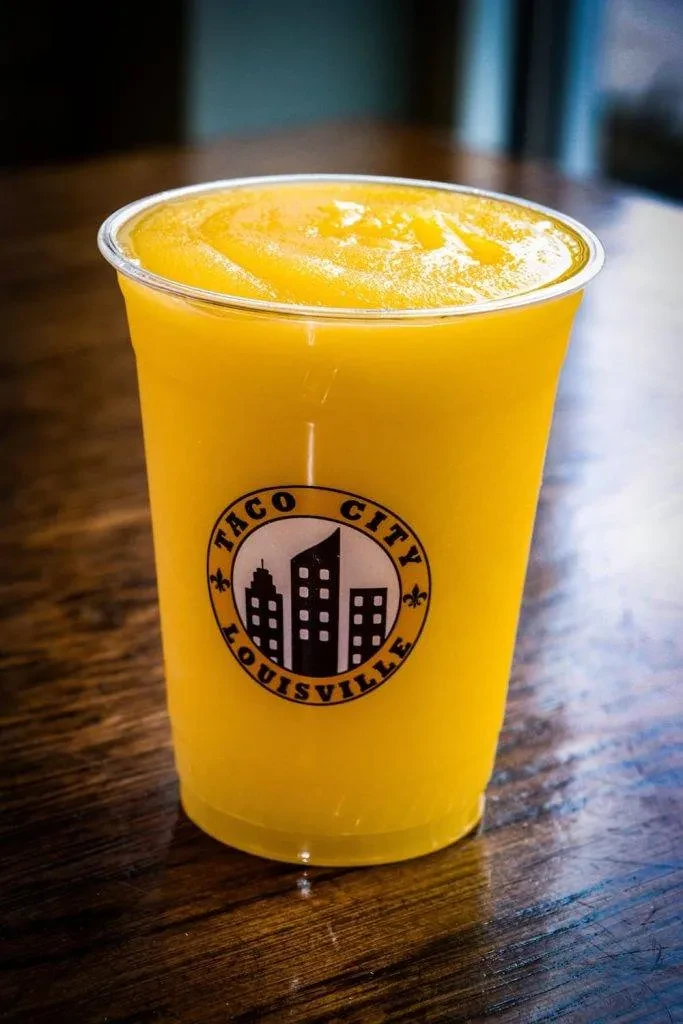 Close-up of a yellow frozen drink with Taco City Louisville logo.