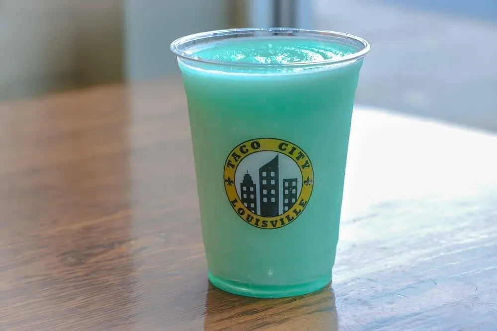 Frothy turquoise frozen drink in a Taco City Louisville cup.