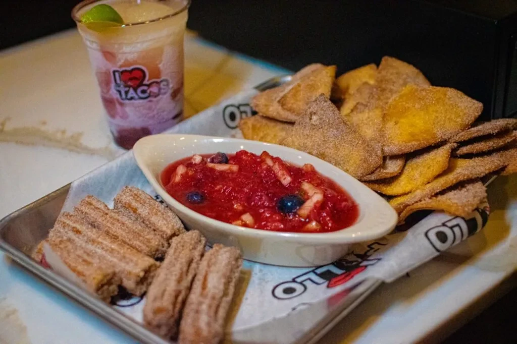 Churros, fruit salsa, cinnamon chips, and a frozen drink on a tray.
