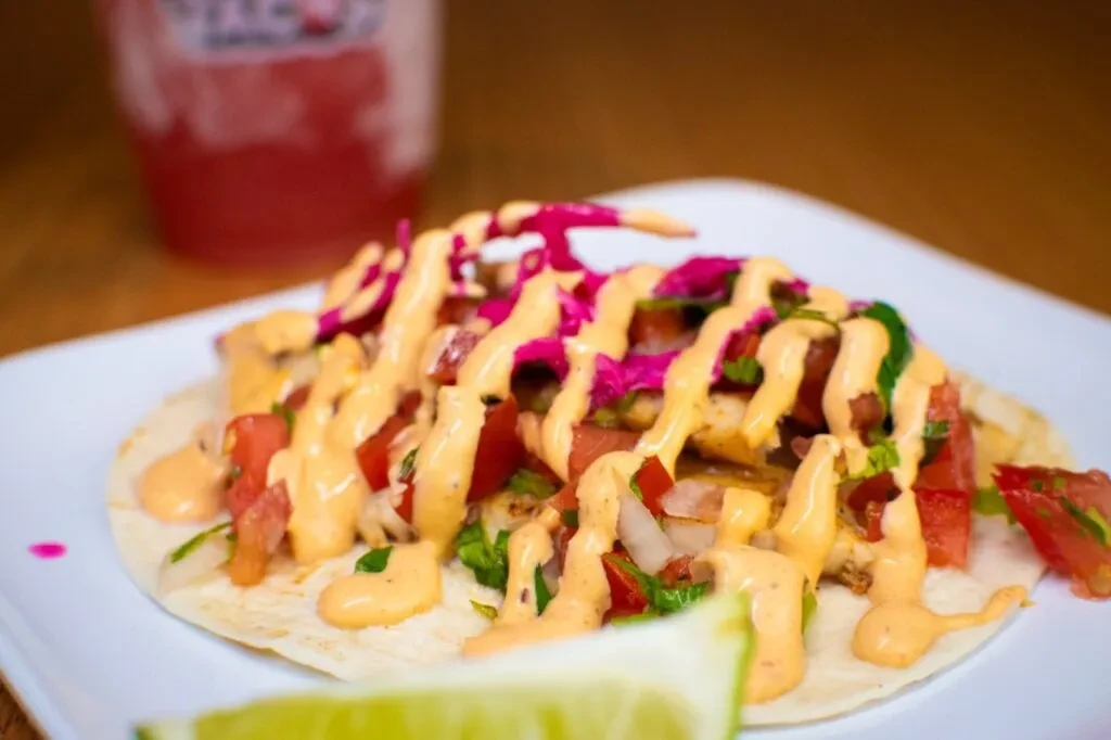 A close-up taco with colorful sauces, lime, on a white plate.
