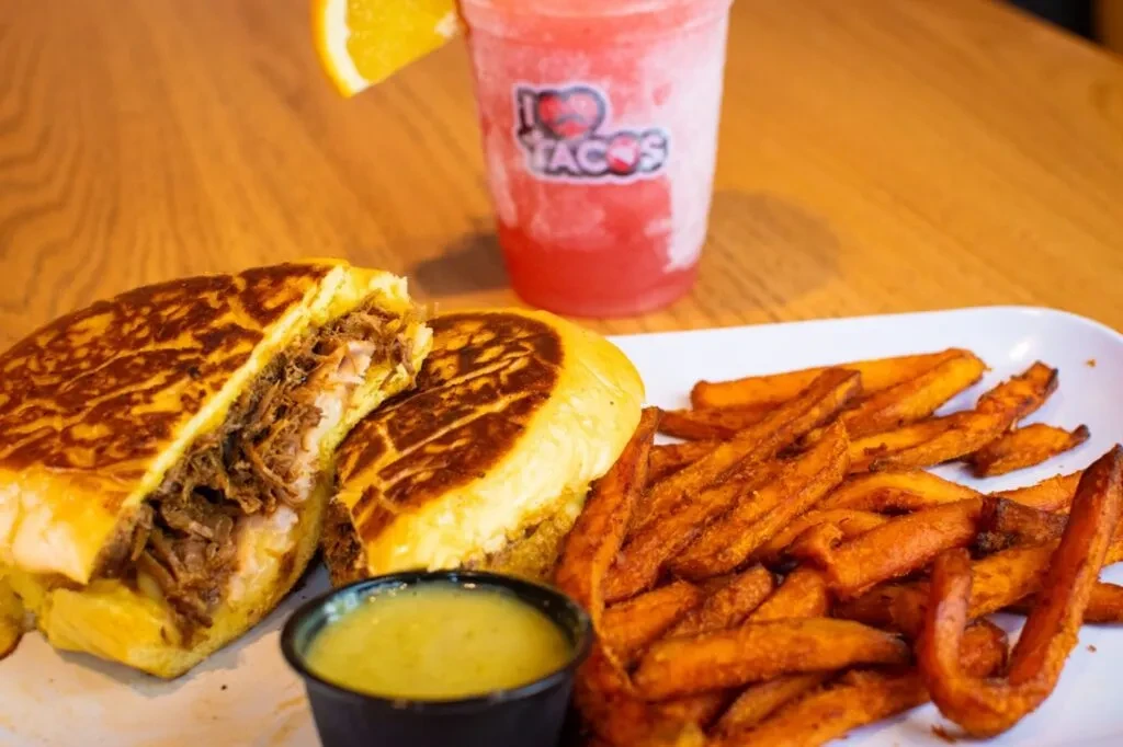 Pressed shredded meat sandwich, sweet potato fries, sauce, and frozen drink.