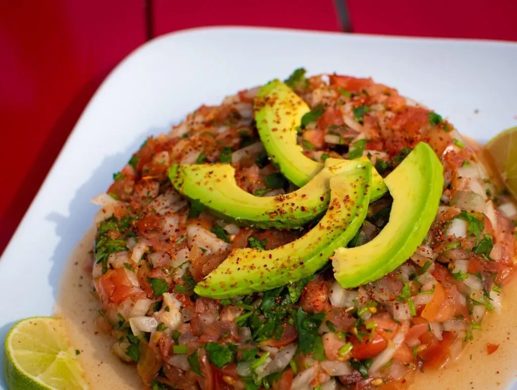 Vibrant chopped vegetable mix with avocado and lime on white plate.