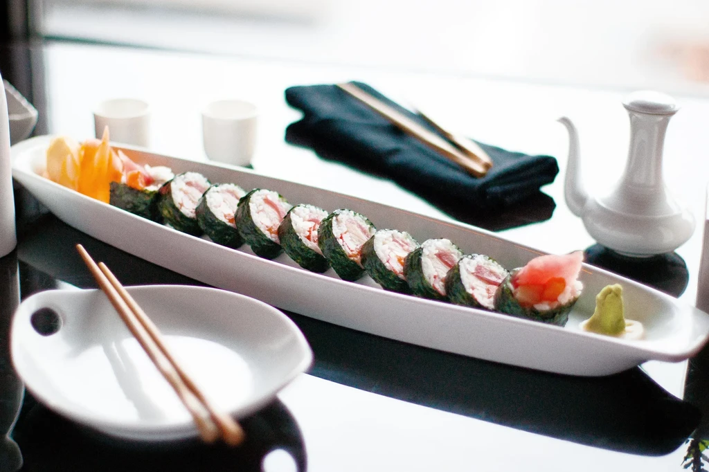 Tuna sushi rolls, pickled ginger, wasabi, orange vegetables, sake, and chopsticks.