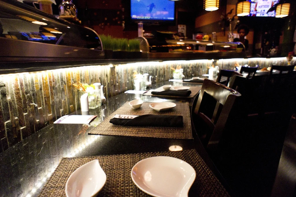 Modern sushi bar counter with warm LED lighting and stone wall.
