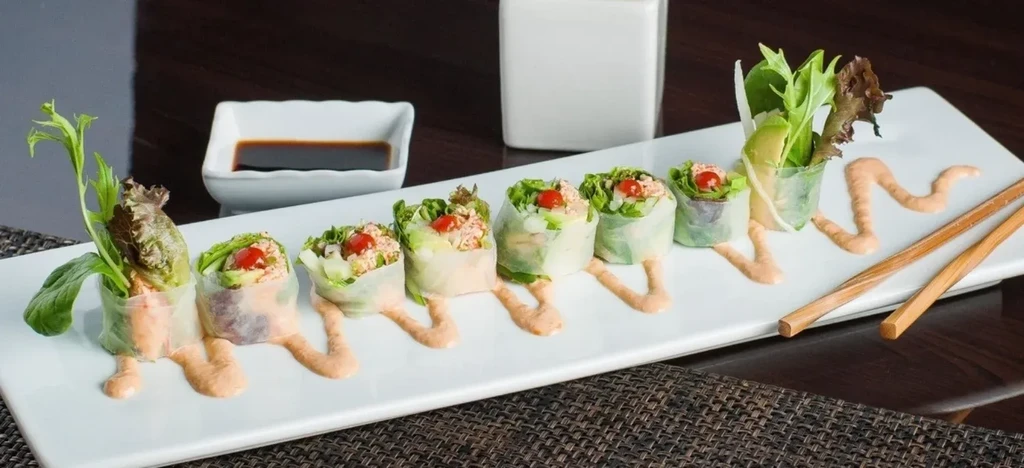 Eight translucent spring rolls, sauce, chopsticks on a white serving plate.