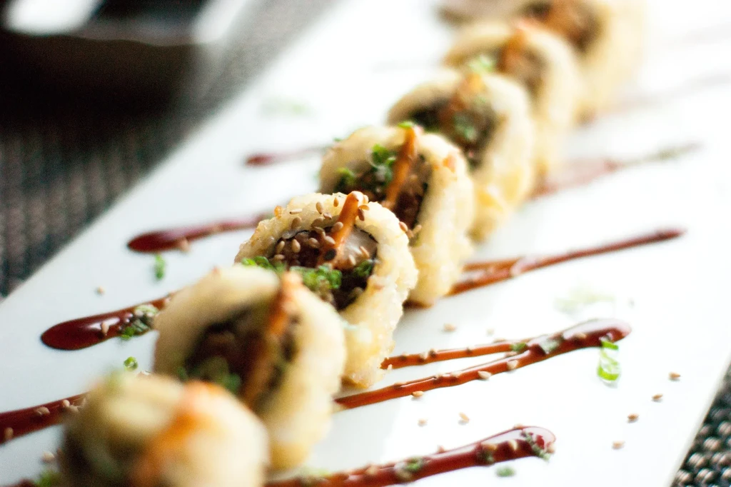 Crispy, golden-brown fried sushi rolls with sauce and garnishes.