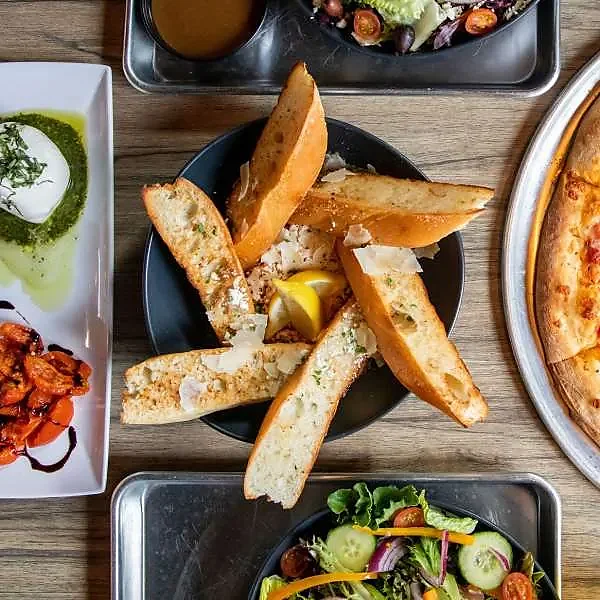 Overhead spread of garlic bread, salads, burrata and pizza on wood