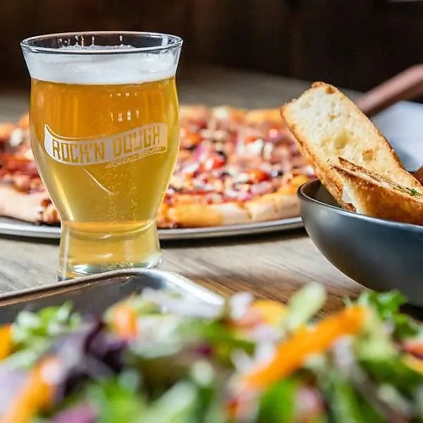 Branded glass of draft beer beside pizza, bread and side salad
