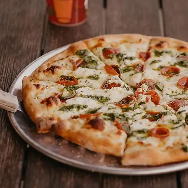 Pepperoni and pesto white pizza on metal pan atop wooden table