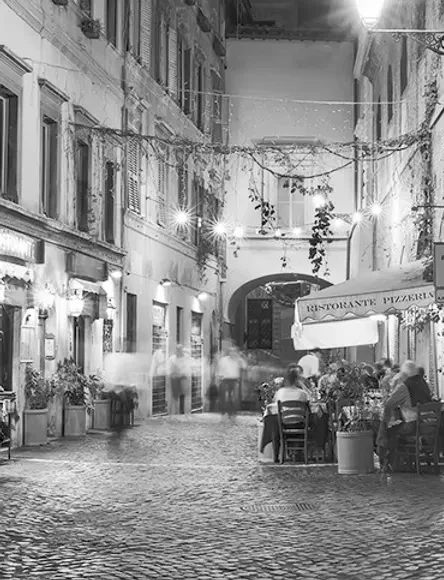B&W photo of a bustling cobblestone street restaurant at night.