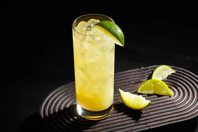 Iced yellowish-green drink with lime on a dark, ridged tray.
