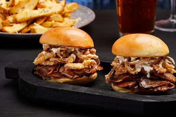 Two sliders with meat, onions, sauce, served with fries and drink.