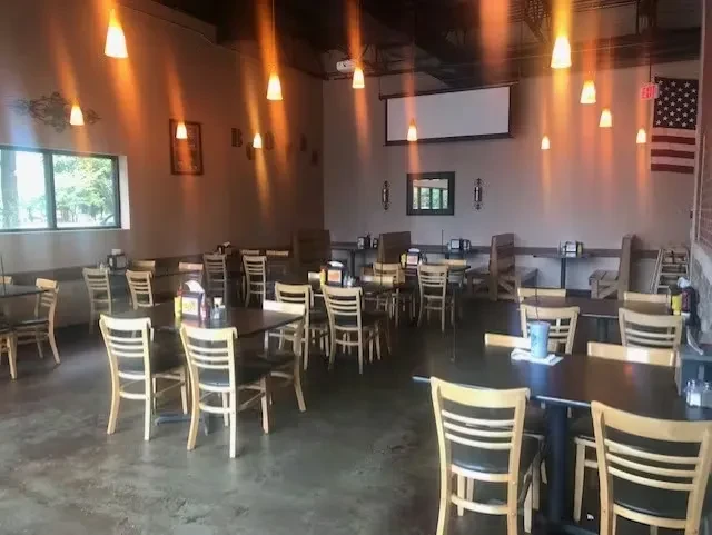 Empty casual restaurant interior with warm lighting, tables, American flag, screen.