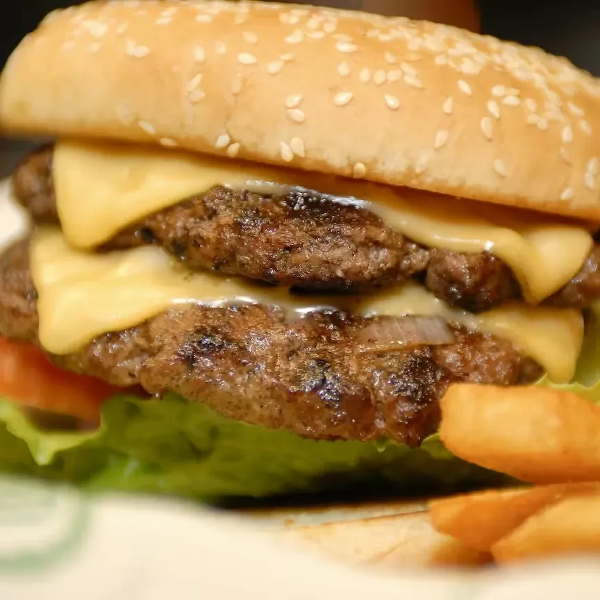Double cheeseburger with melted cheese, grilled patties, lettuce, tomato, fries.