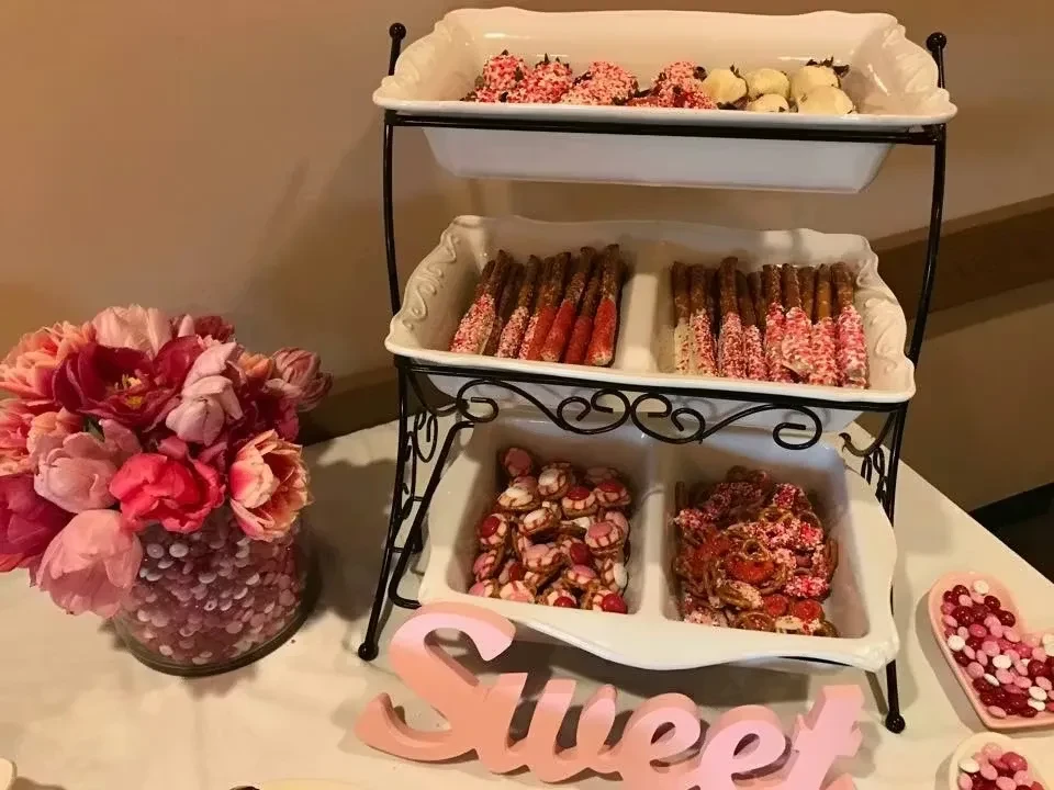 Three-tiered stand holding chocolate treats, pretzel sticks, candies, and flowers.