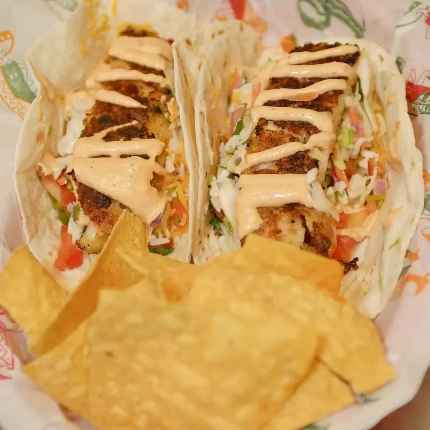 Two fish tacos with slaw, creamy sauce, and tortilla chips.