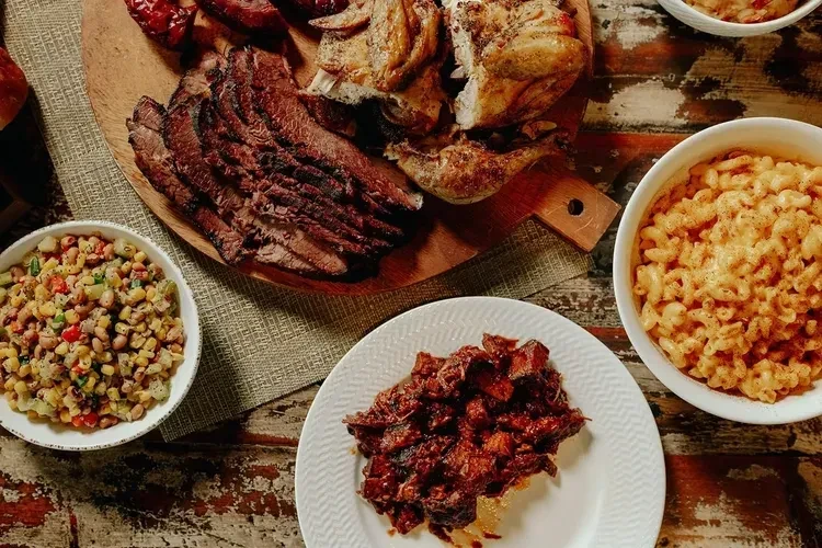Barbecue feast with brisket, chicken, mac and cheese on a wooden table.