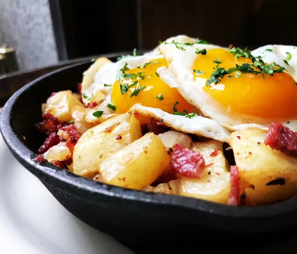 Corned beef hash with two sunny-side-up eggs in a dark skillet.