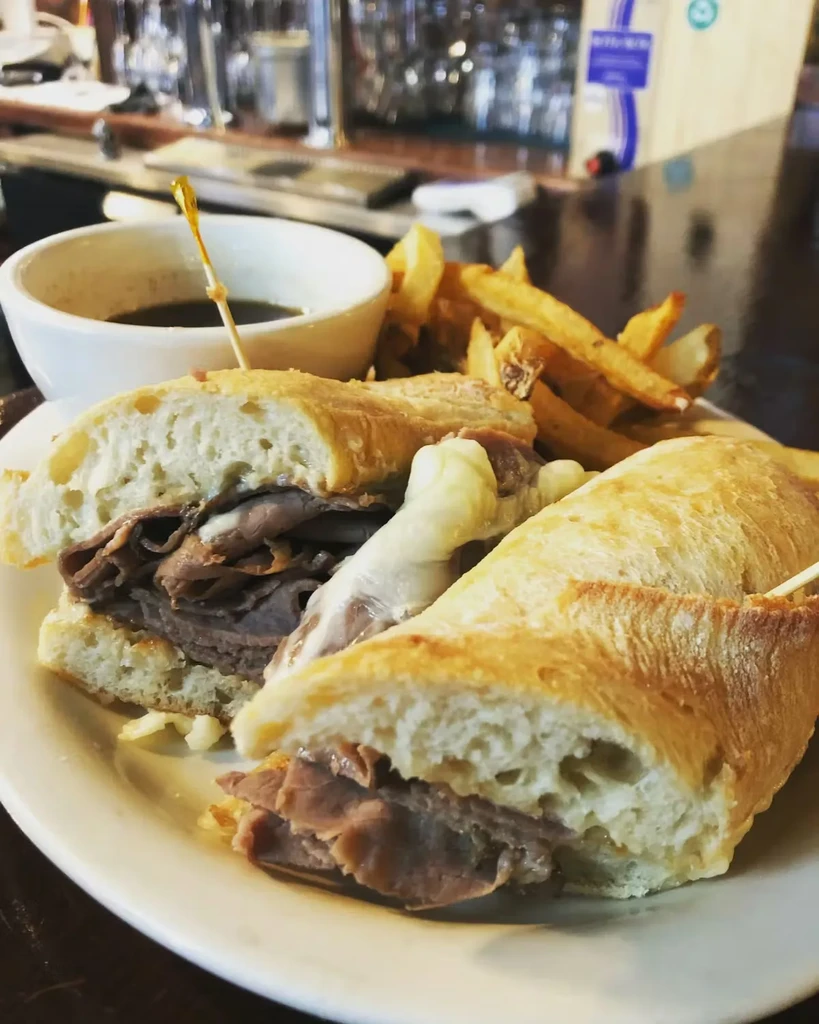 Close-up: Roast beef baguette sandwich with melted cheese, au jus, and fries.